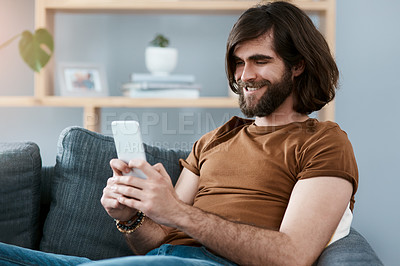Buy stock photo Shot of a handsome young man using his cellphone while relaxing on a sofa in his living room