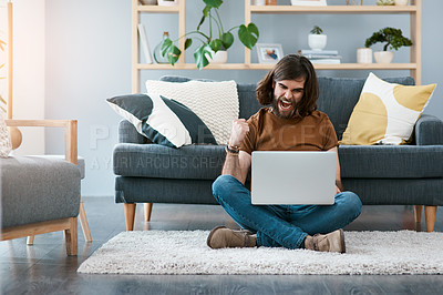 Buy stock photo Shot of a cheerful young man using his laptop while sitting on a carpet in his living room