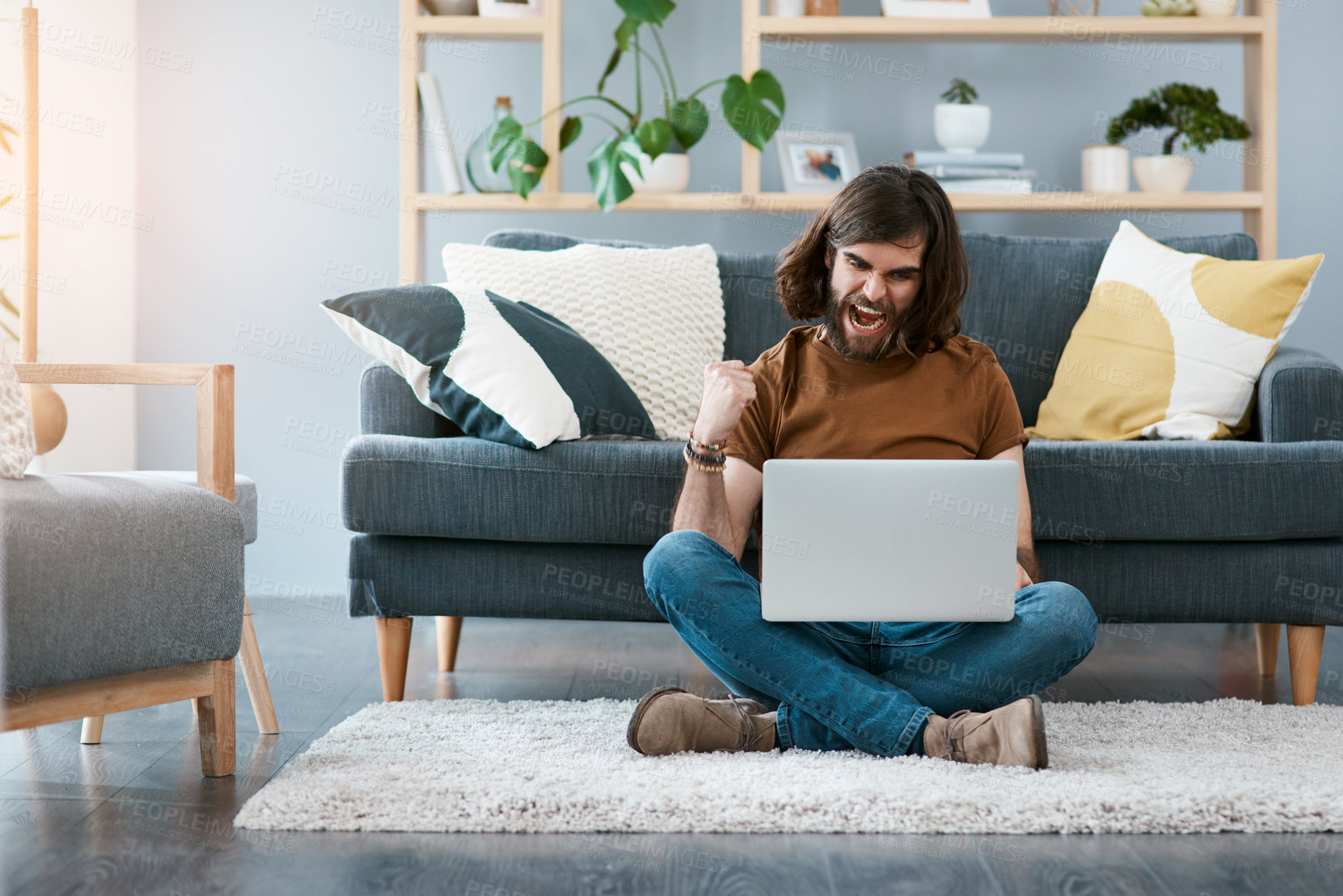 Buy stock photo Shot of a cheerful young man using his laptop while sitting on a carpet in his living room