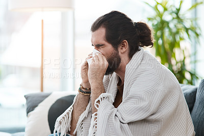 Buy stock photo Shot of a sickly young man blowing his nose with a tissue in his living room