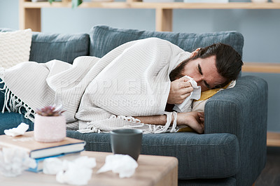Buy stock photo Shot of a sickly young man blowing his nose with a tissue in his living room