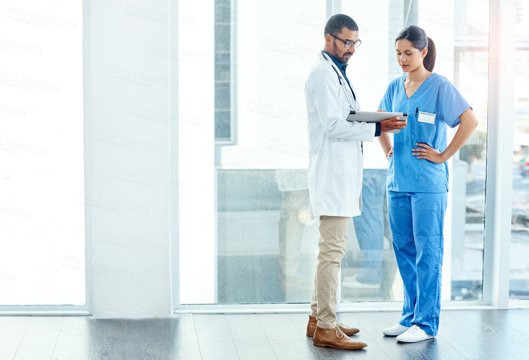 Buy stock photo Shot of two young doctors using a digital tablet in a modern hospital