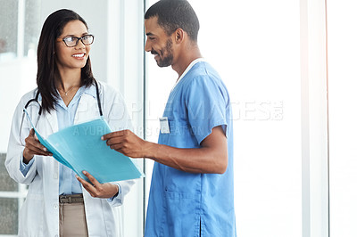 Buy stock photo Shot of two young doctors discussing the contents of a file in a modern hospital