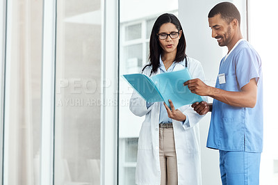 Buy stock photo Shot of two young doctors discussing the contents of a file in a modern hospital