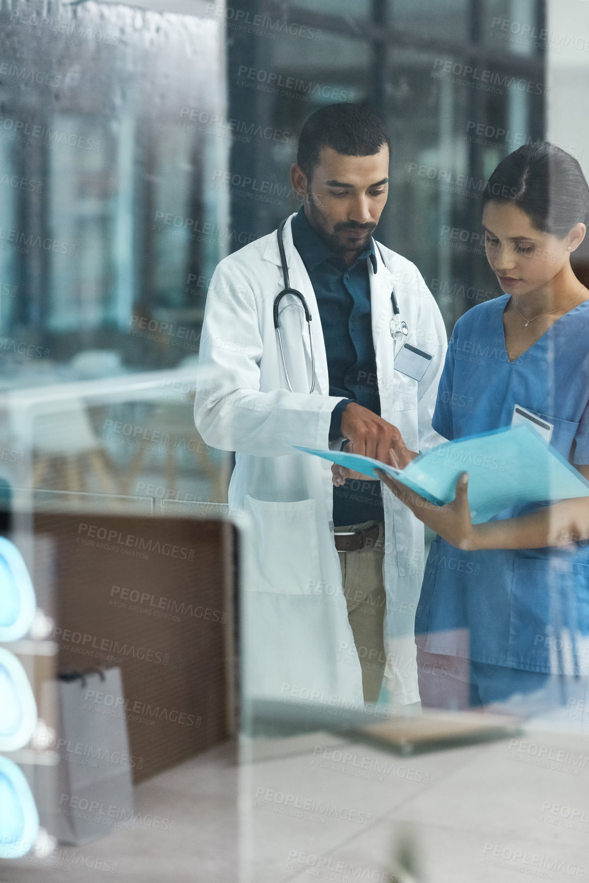 Buy stock photo Shot of two young doctors discussing the contents of a file in a modern hospital