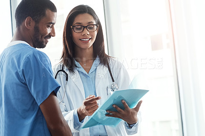 Buy stock photo Shot of two young doctors discussing the contents of a file in a modern hospital