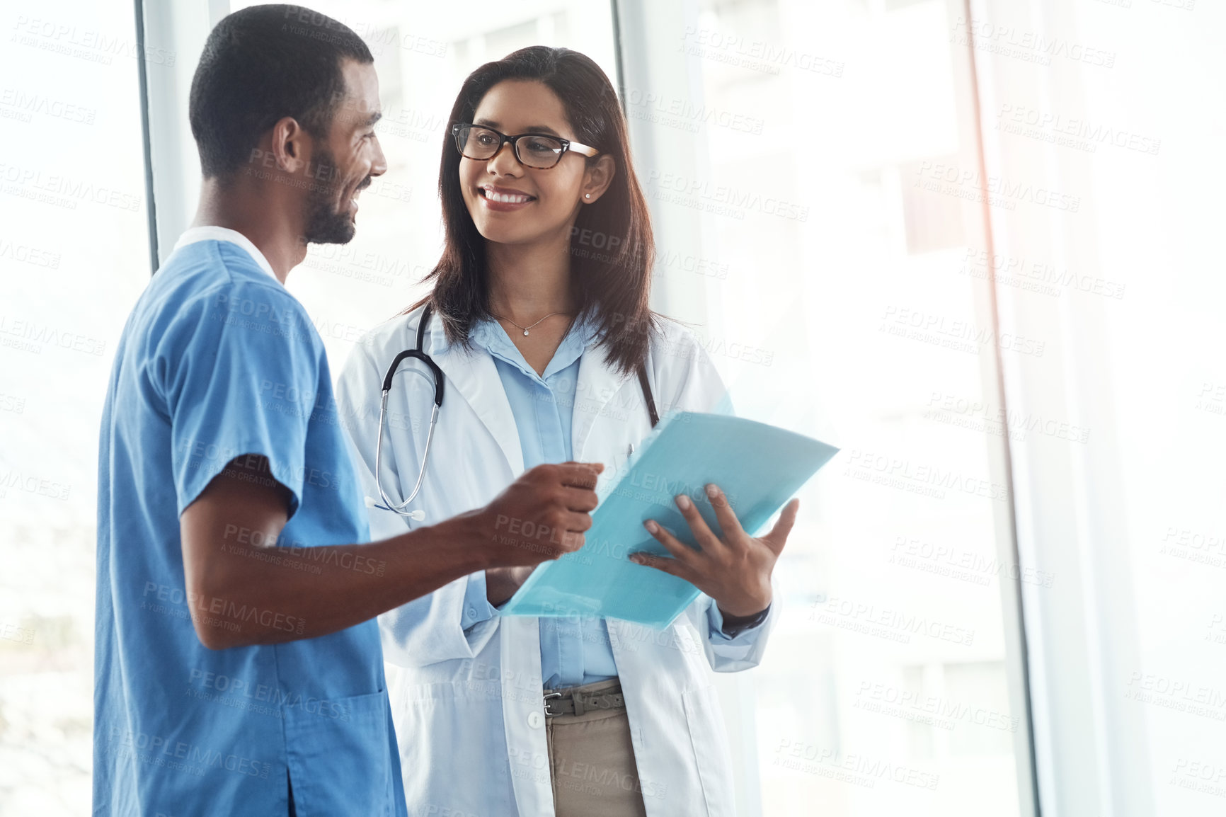 Buy stock photo Shot of two young doctors discussing the contents of a file in a modern hospital