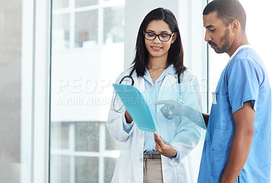 Buy stock photo Shot of two young doctors discussing the contents of a file in a modern hospital