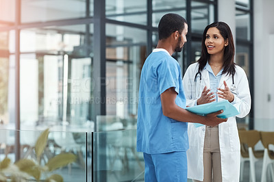 Buy stock photo Shot of two young doctors discussing the contents of a file in a modern hospital