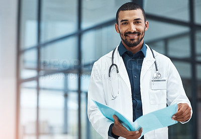 Buy stock photo Portrait of a young doctor going over the contents of a file in a modern hospital