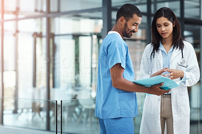 Buy stock photo Shot of two young doctors discussing the contents of a file in a modern hospital