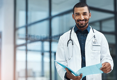 Buy stock photo Portrait of a young doctor going over the contents of a file in a modern hospital