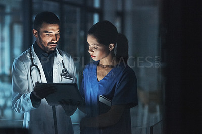 Buy stock photo Shot of two young doctors using a digital tablet late at night in a modern hospital