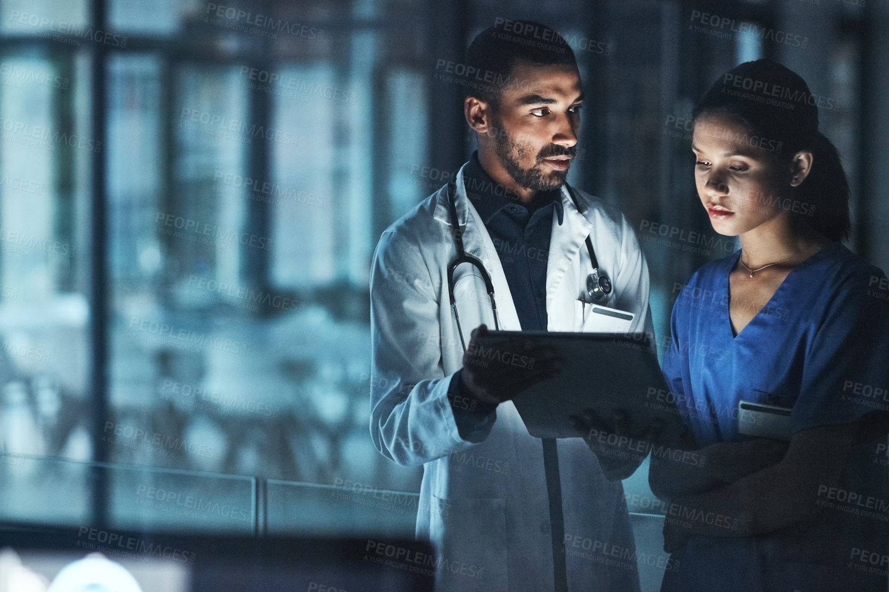 Buy stock photo Shot of two young doctors using a digital tablet late at night in a modern hospital