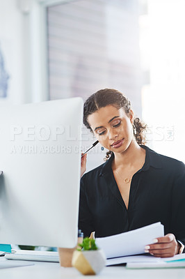 Buy stock photo Shot of a young businesswoman going through paperwork while working in an office