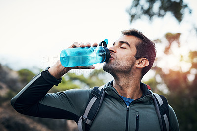 Buy stock photo Cropped shot of a carefree young man drinking water from a bottle while going for a hike up a mountain