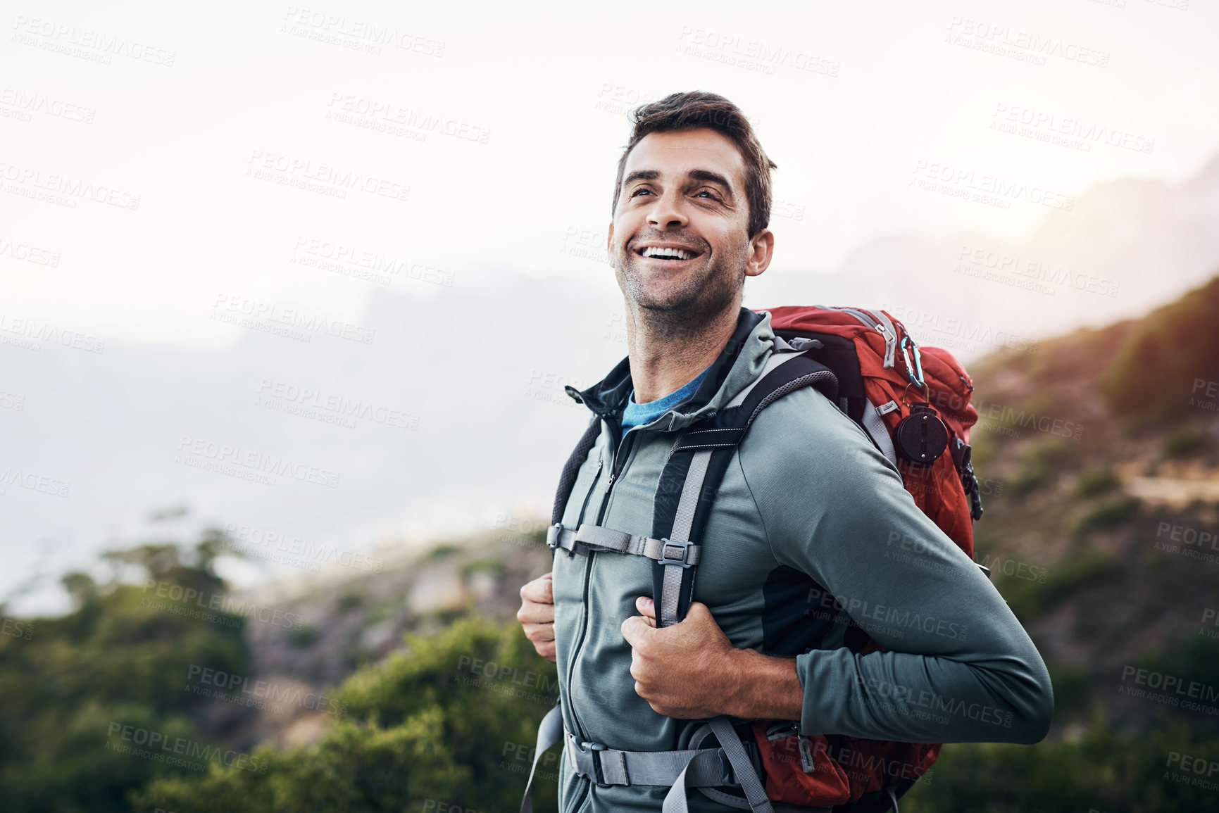 Buy stock photo Cropped shot of a cheerful young man looking into the distance while going for a hike up a mountain