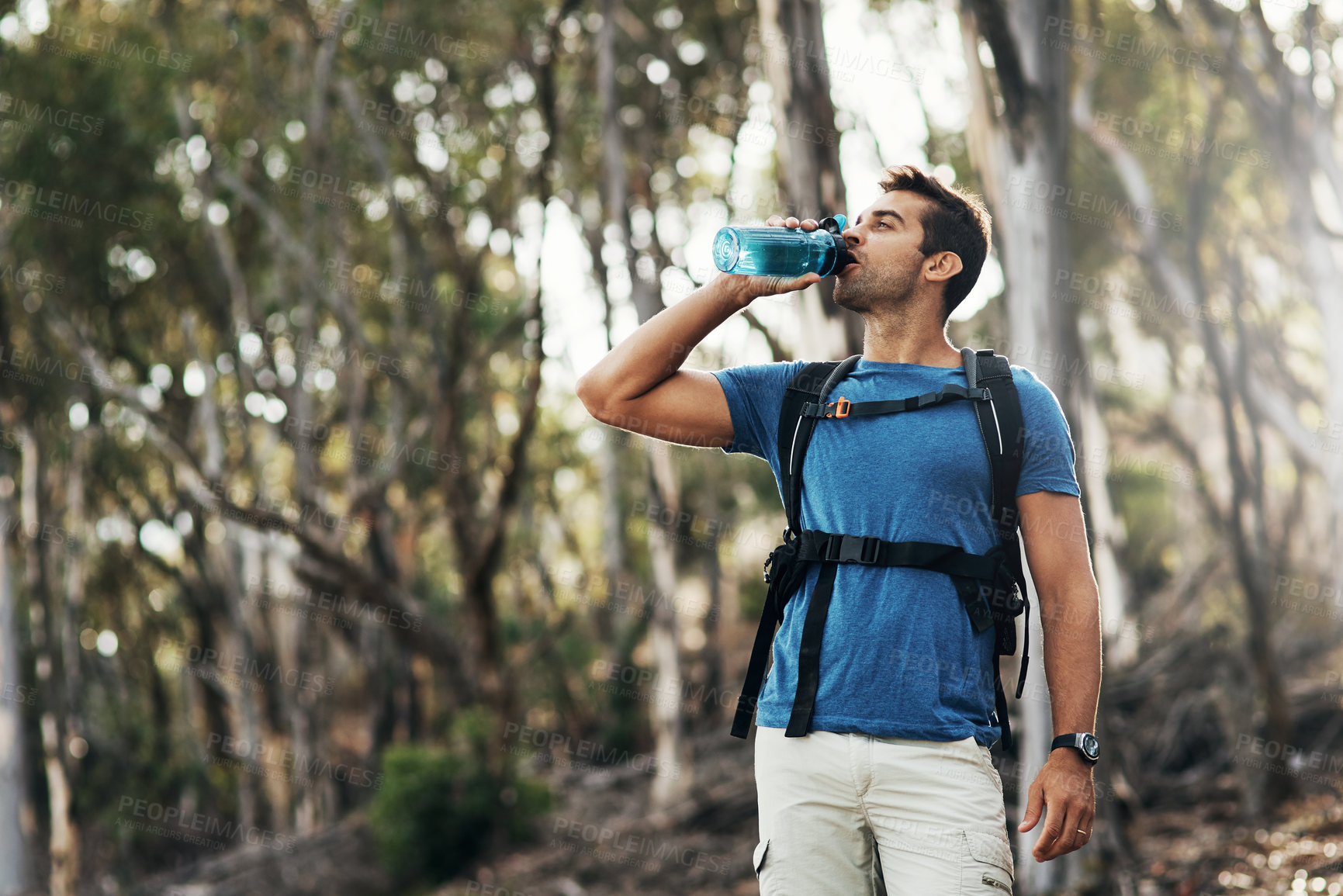 Buy stock photo Cropped shot of a carefree young man drinking water from a bottle while going for a hike up a mountain