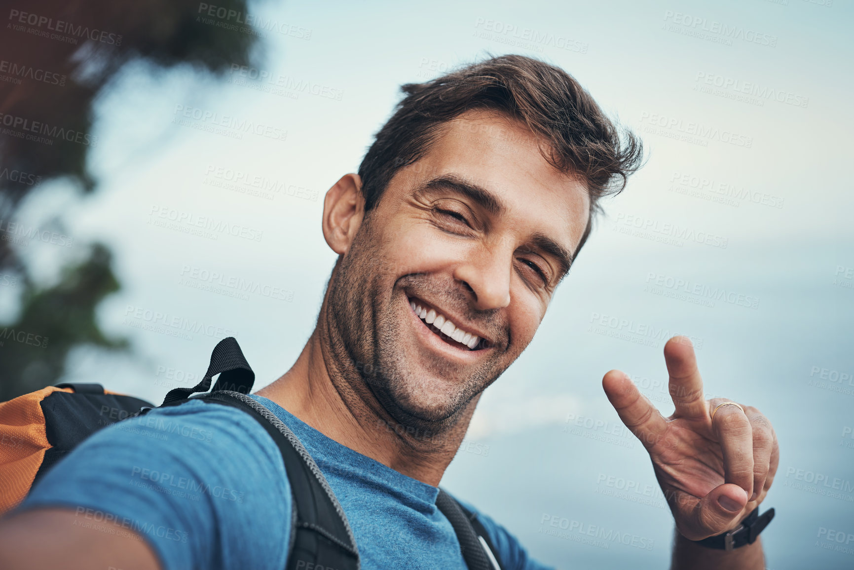 Buy stock photo Portrait of a cheerful young man showing the peace sign while going for a hike up a mountain