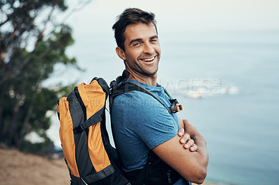 Buy stock photo Portrait of a cheerful young man standing with his arms folded while going for a hike up a mountain