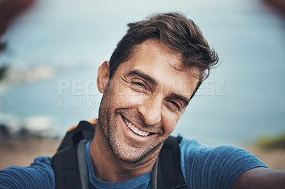 Buy stock photo Portrait of a cheerful young man taking a self portrait with his cellphone while going for a hike up a mountain