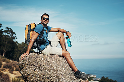 Buy stock photo Portrait of a carefree young man taking a quick break from hiking up a mountain during the day