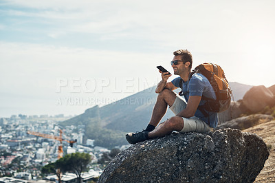 Buy stock photo Cropped shot of a carefree young man seated on top of a mountain while talking on his cellphone outside during the day