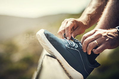 Buy stock photo Cropped shot of an unrecognizable young man tying his laces during a hike in the mountains