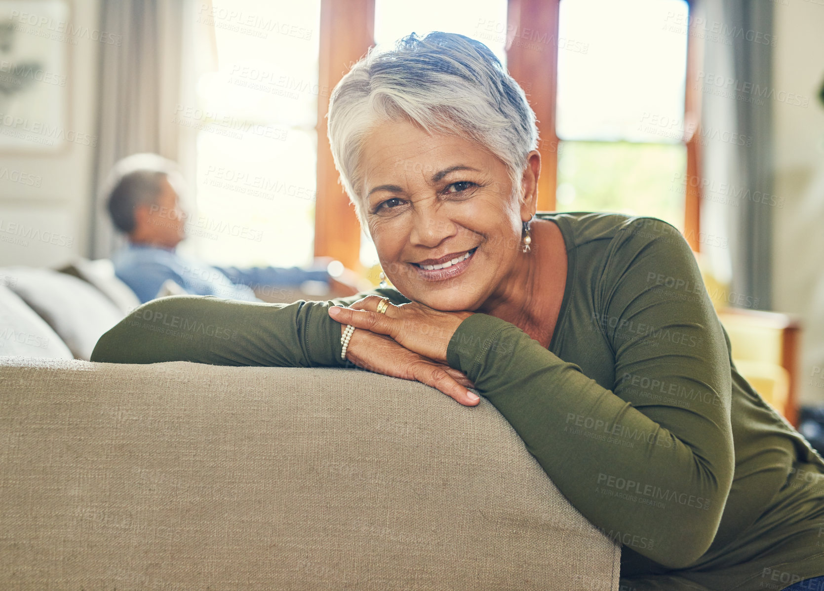 Buy stock photo Portrait of a beautiful senior woman relaxing on a couch with her husband in the background
