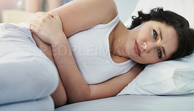 Buy stock photo Cropped shot of an attractive young woman suffering with stomach cramps while lying in bed at home