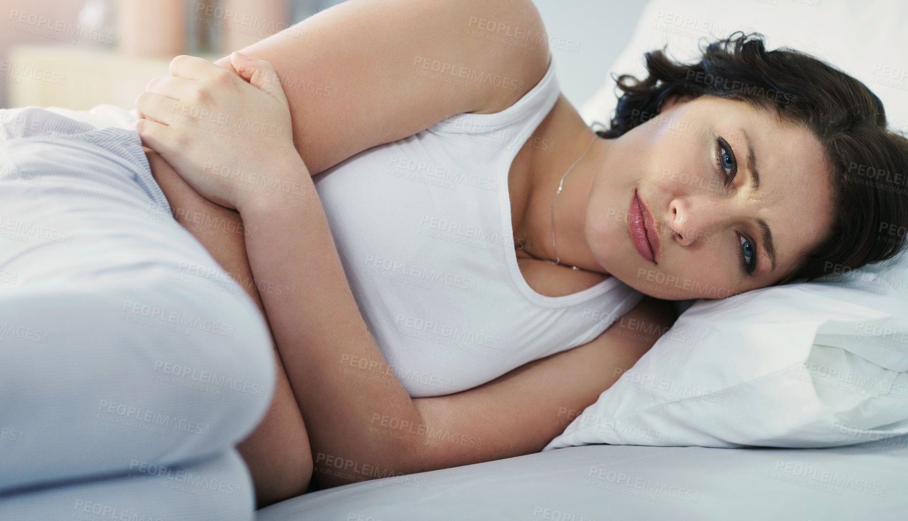 Buy stock photo Cropped shot of an attractive young woman suffering with stomach cramps while lying in bed at home