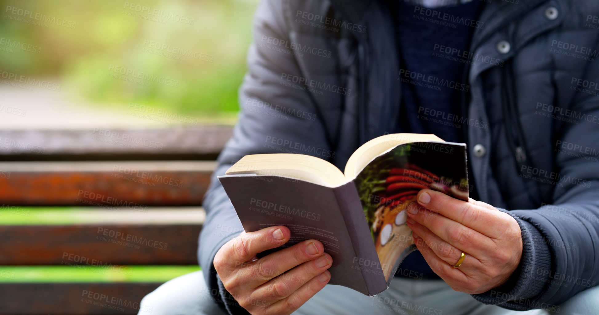 Buy stock photo Cropped shot of an unrecognizable elderly man reading a book by herself outside in a park