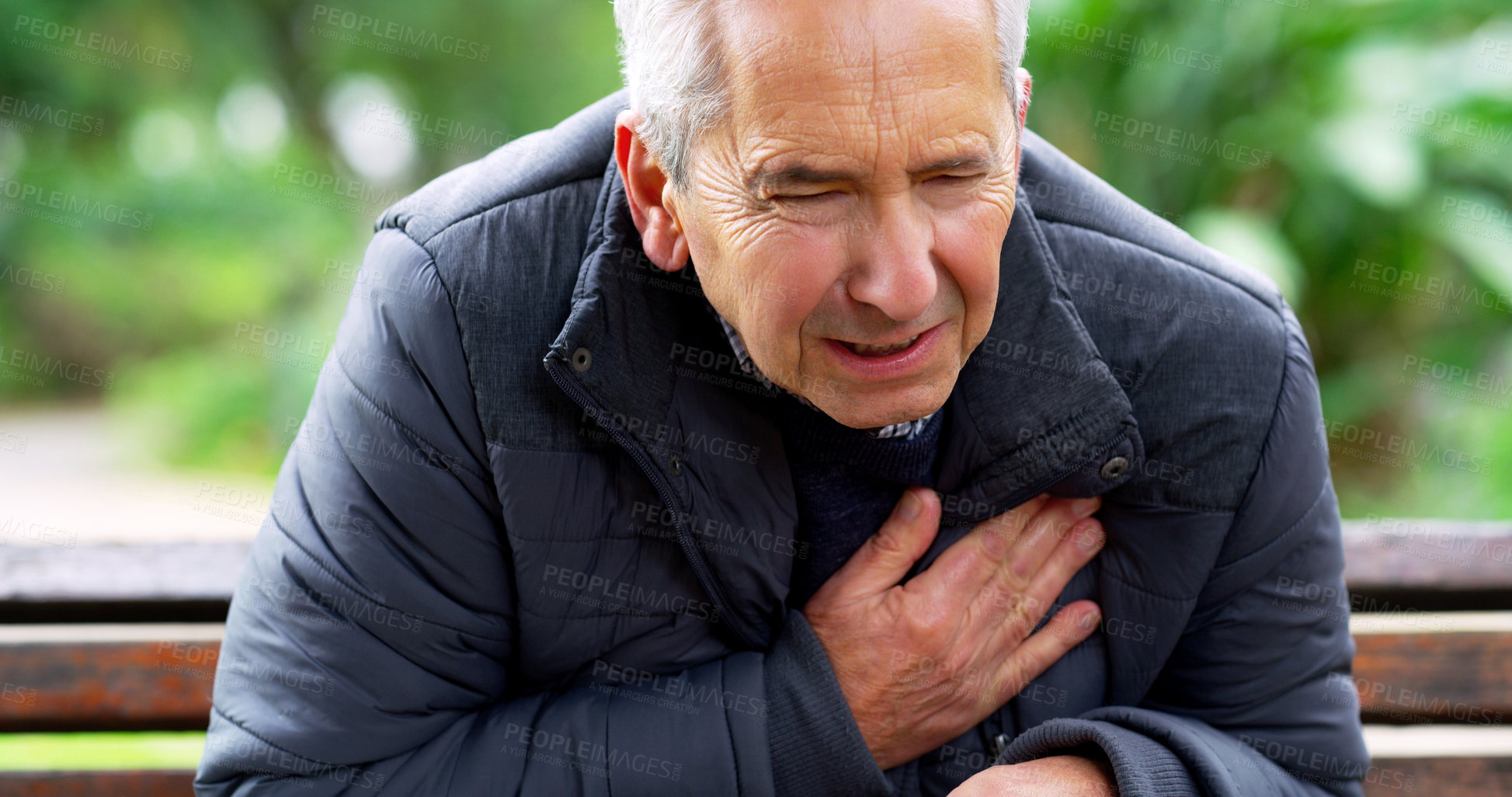 Buy stock photo Cropped shot of a stressed out elderly man seated on a bench and holding his chest in discomfort outside in a park