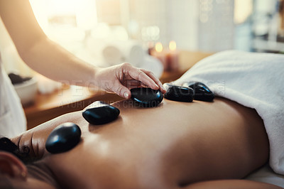Buy stock photo Woman, hands and rocks for back massage at spa in beauty relaxation or skincare on bed. Hand of masseuse applying hot rock or stones on female for physical therapy, zen or skin treatment at resort