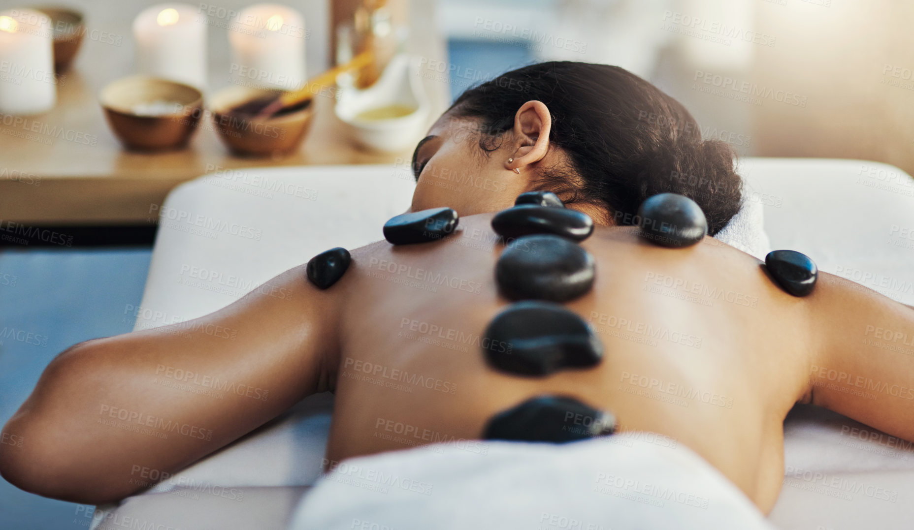 Buy stock photo Woman, relax and rock massage at spa for skincare, beauty or body treatment on bed at resort. Calm female lying in relaxation with hot rocks or stone pile on back in therapy, zen or wellness at salon