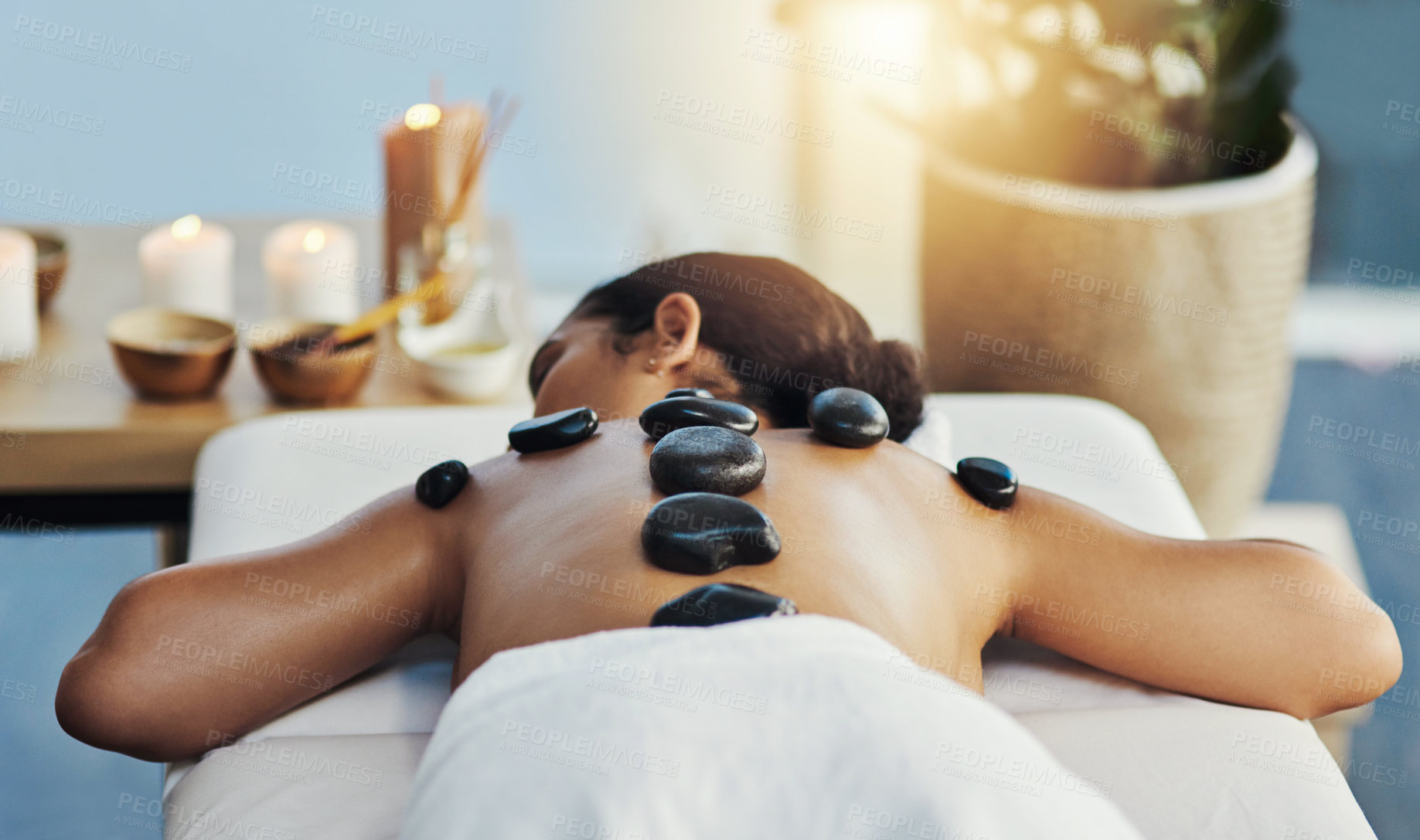 Buy stock photo Woman, relax and rock in back massage at spa for skincare, beauty or body treatment on bed at resort. Calm female lying in relaxation with hot rocks or stone pile in therapy, zen or wellness at salon