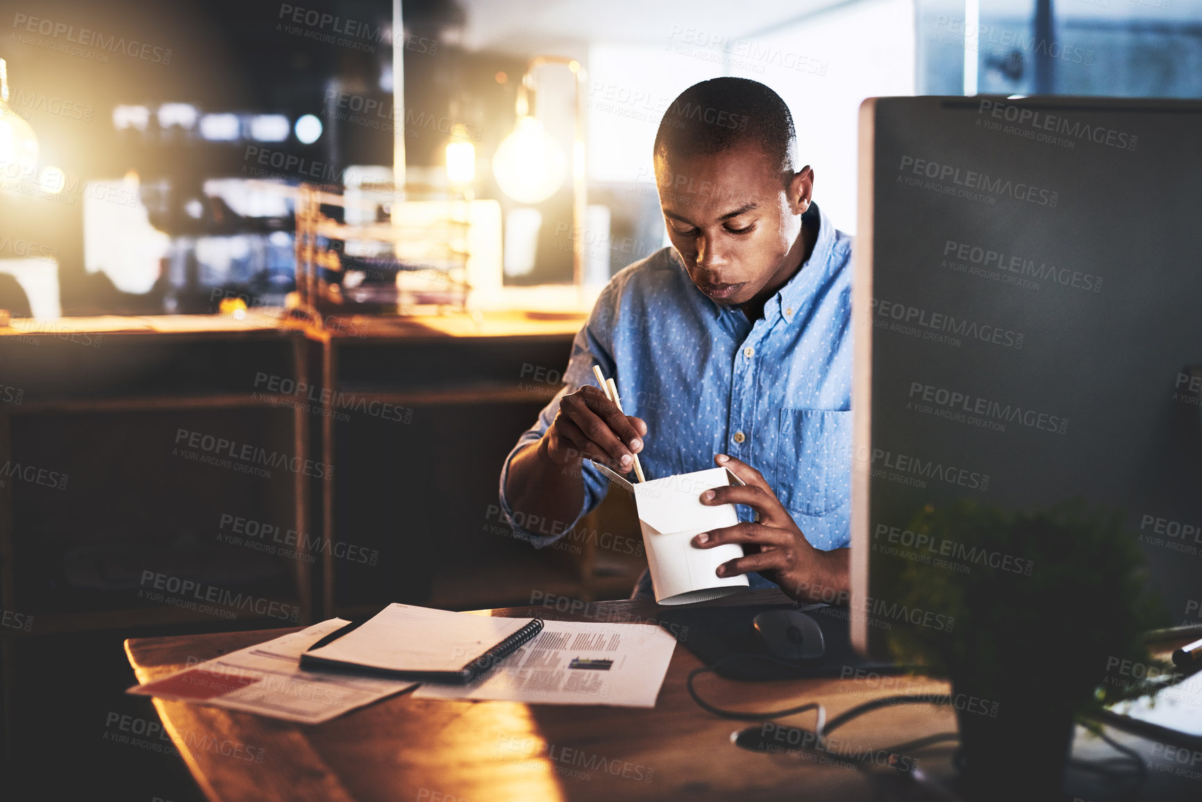 Buy stock photo Cropped shot of a handsome young businessman eating takeout at his desk while working at night in a modern office