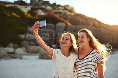 Buy stock photo Shot of two friends taking a selfie while spending the day at the beach