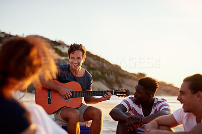 Buy stock photo Shot of a man playing the guitar while sitting on the beach with his friends