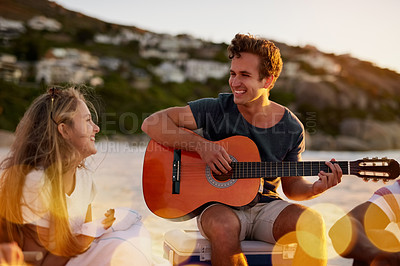 Buy stock photo Shot of a man playing the guitar while sitting on the beach with his girlfriend