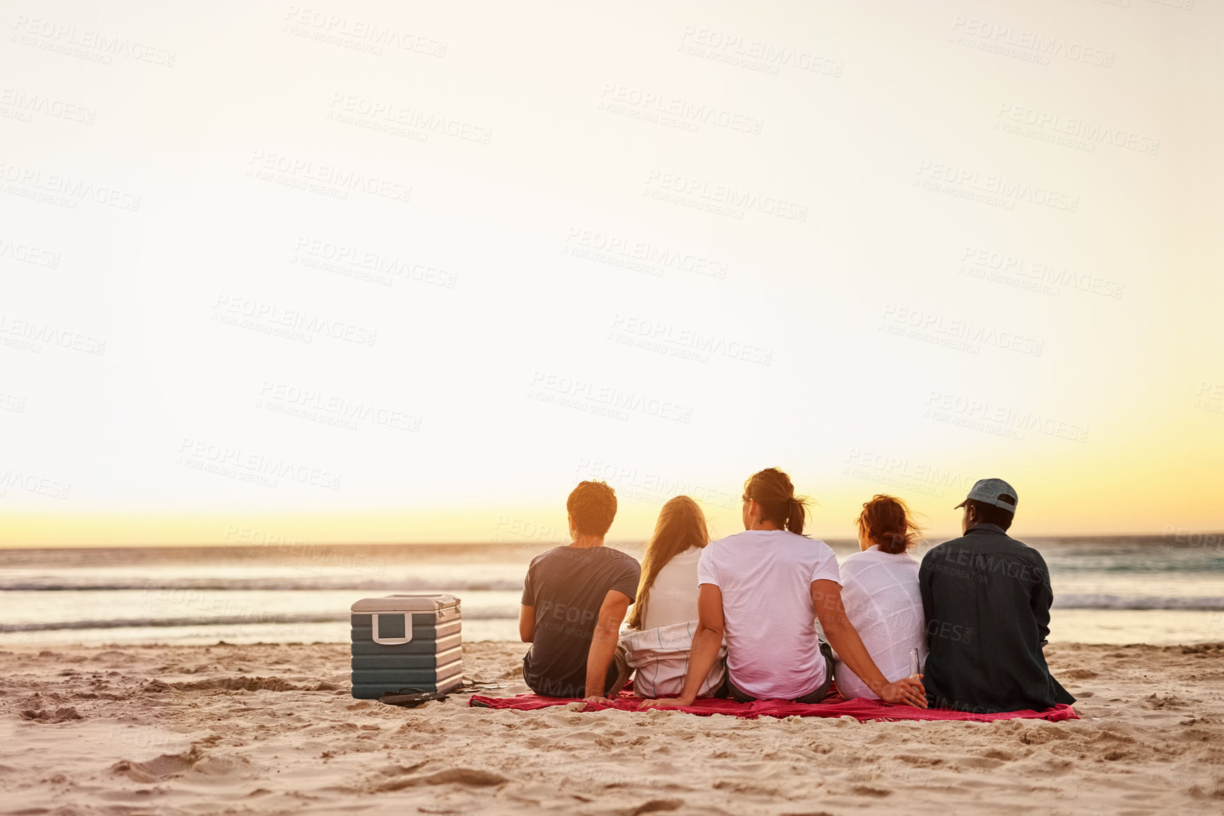 Buy stock photo Rearview shot of a group of friends watching the sunset on the beach