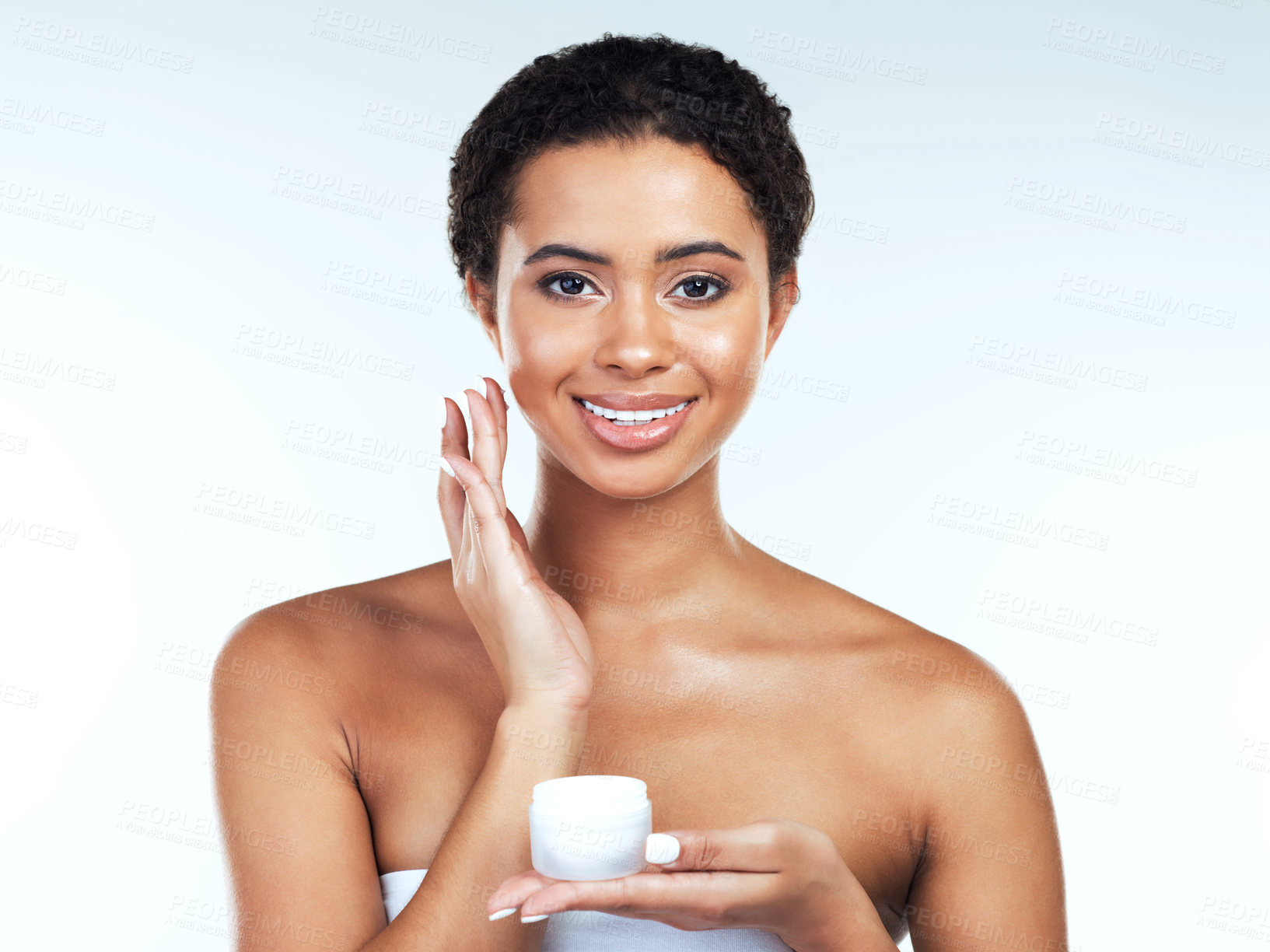 Buy stock photo Portrait of an attractive young woman posing while applying cream to her face  against a white background