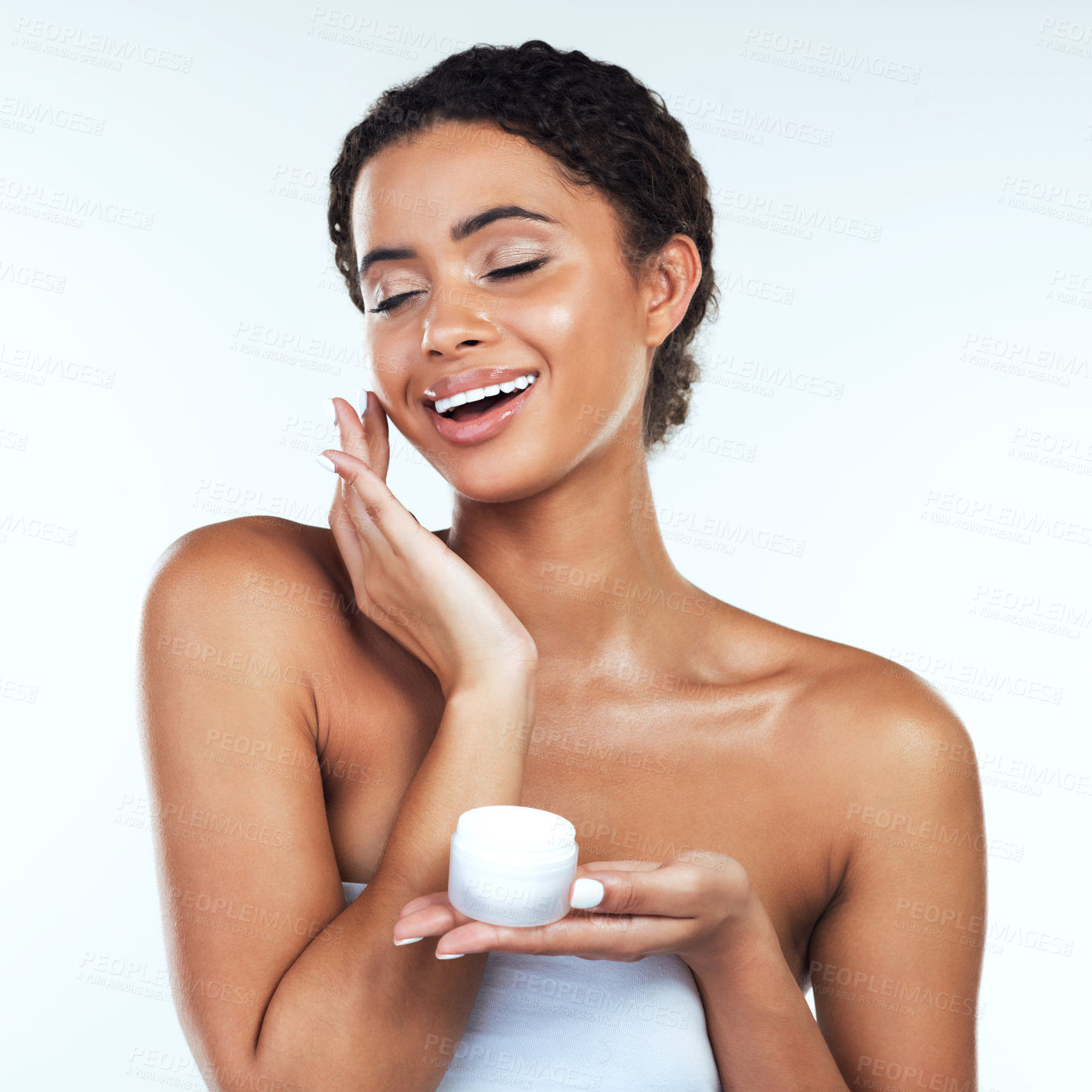 Buy stock photo Studio shot of an attractive young woman posing while applying cream to her face  against a white background