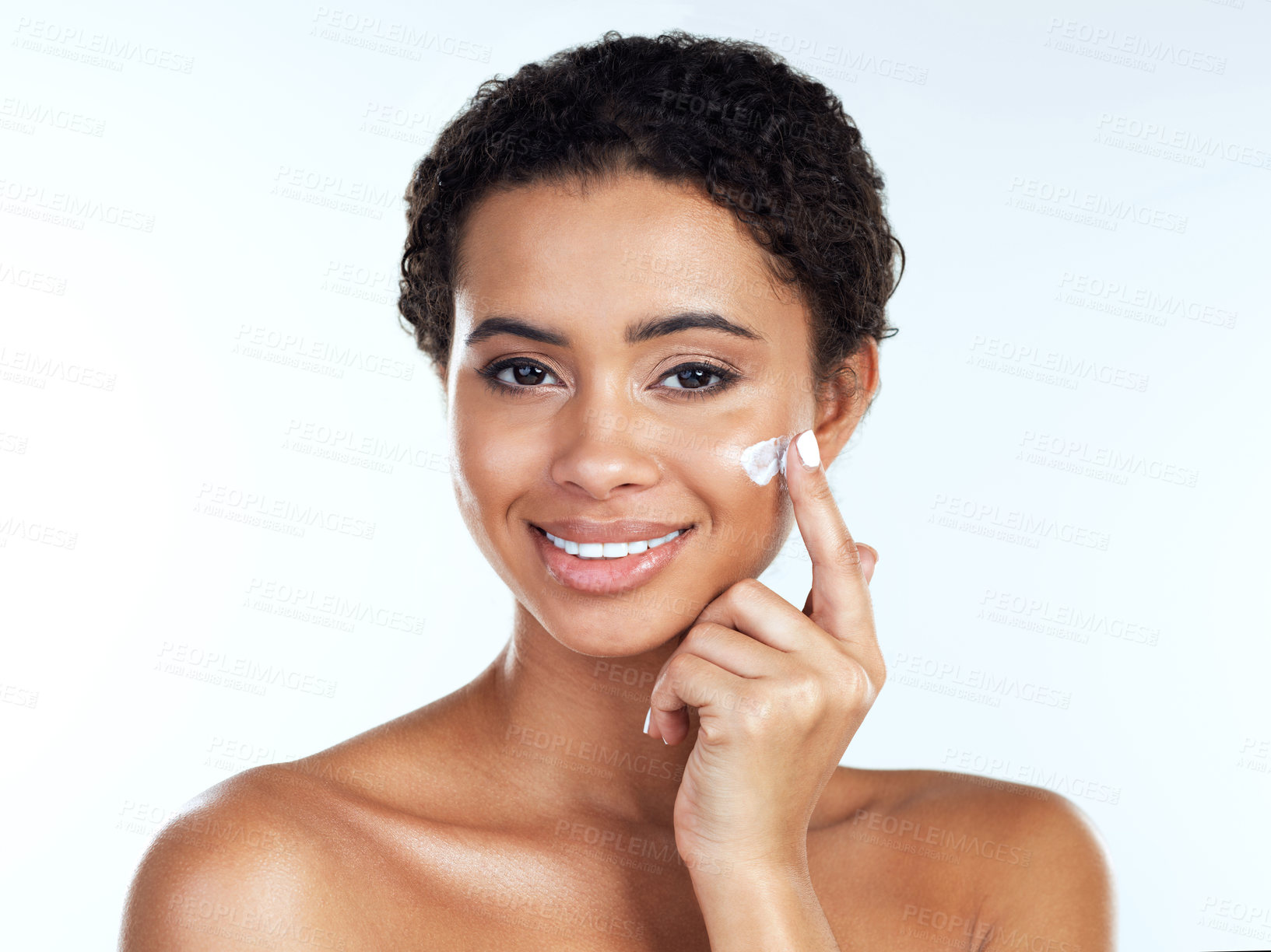 Buy stock photo Portrait of an attractive young woman posing while applying cream to her face  against a white background
