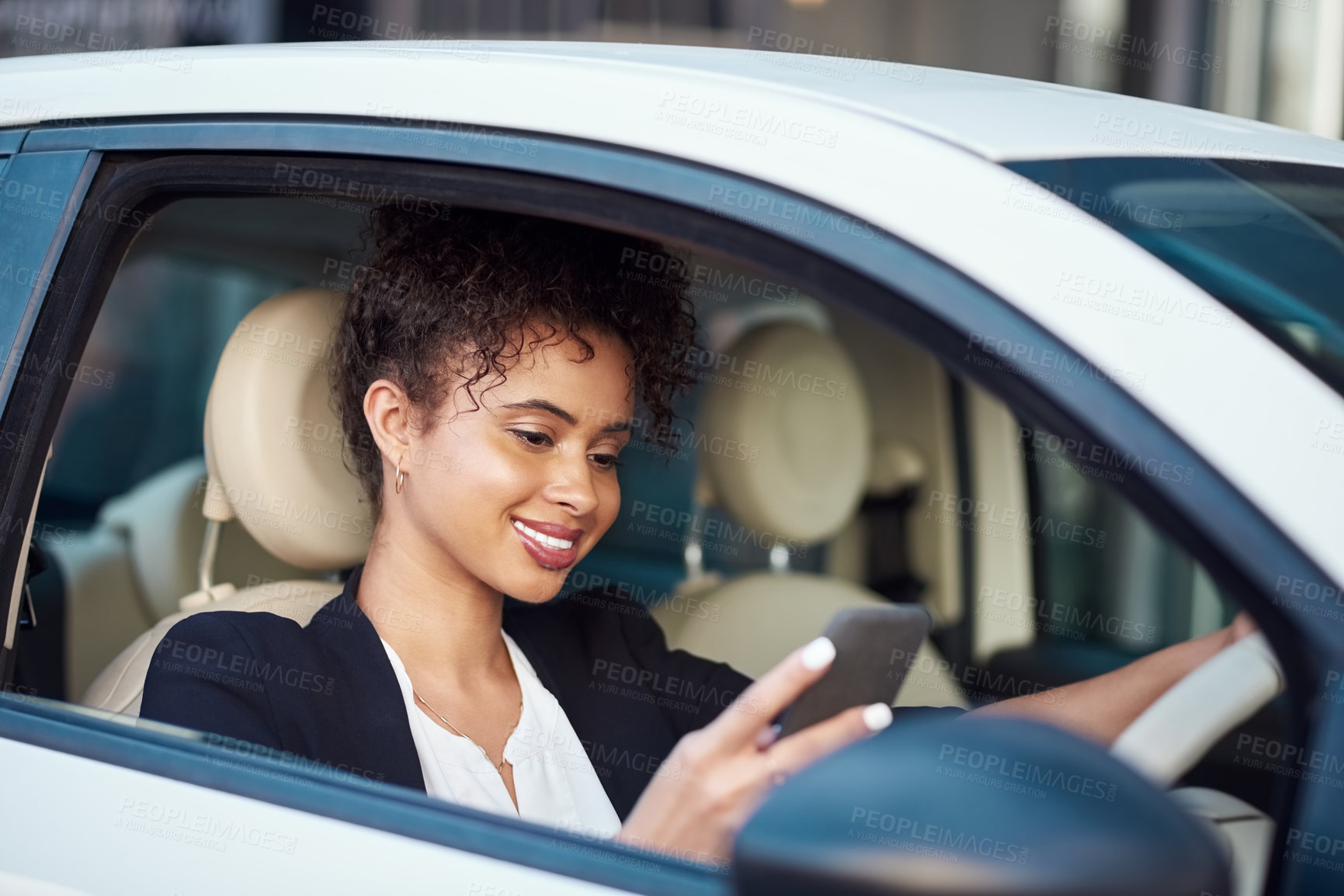 Buy stock photo Cropped shot of an attractive young businesswoman using a smartphone while driving her car