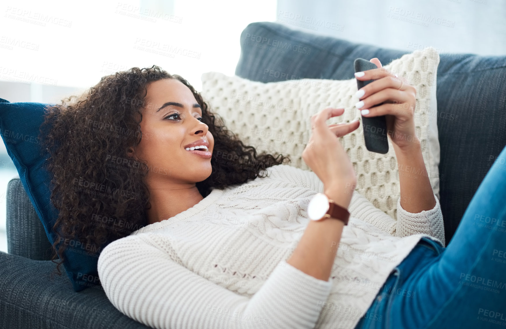 Buy stock photo Shot of a young woman using her cellphone while relaxing at home