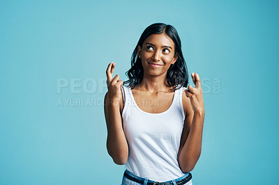 Buy stock photo Smile, fingers crossed and woman in studio for wish, optimism or good luck sign or emoji. Happy, pride and Indian female person with hope hand gesture for superstition isolated by blue background.