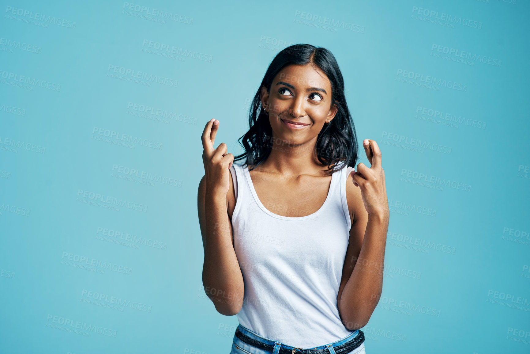 Buy stock photo Studio shot of a beautiful young woman crossing her fingers against a blue background