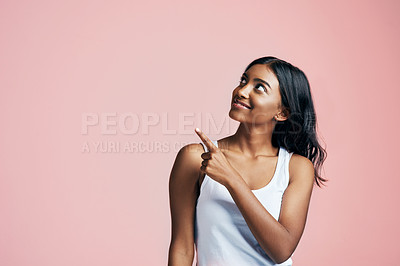 Buy stock photo Studio shot of a beautiful young woman pointing towards copyspace against a pink background