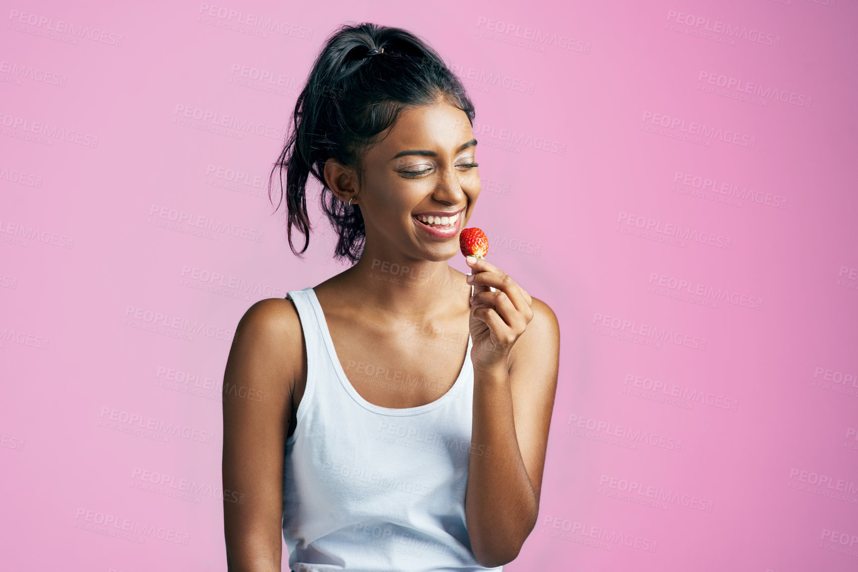 Buy stock photo Studio shot of a beautiful young woman eating a strawberry against a pink background